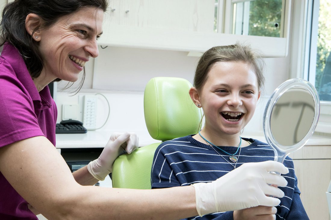 Kieferorthopädische Behandlung: eine Patientin betrachtet ihre Zahnspange im Handspiegel