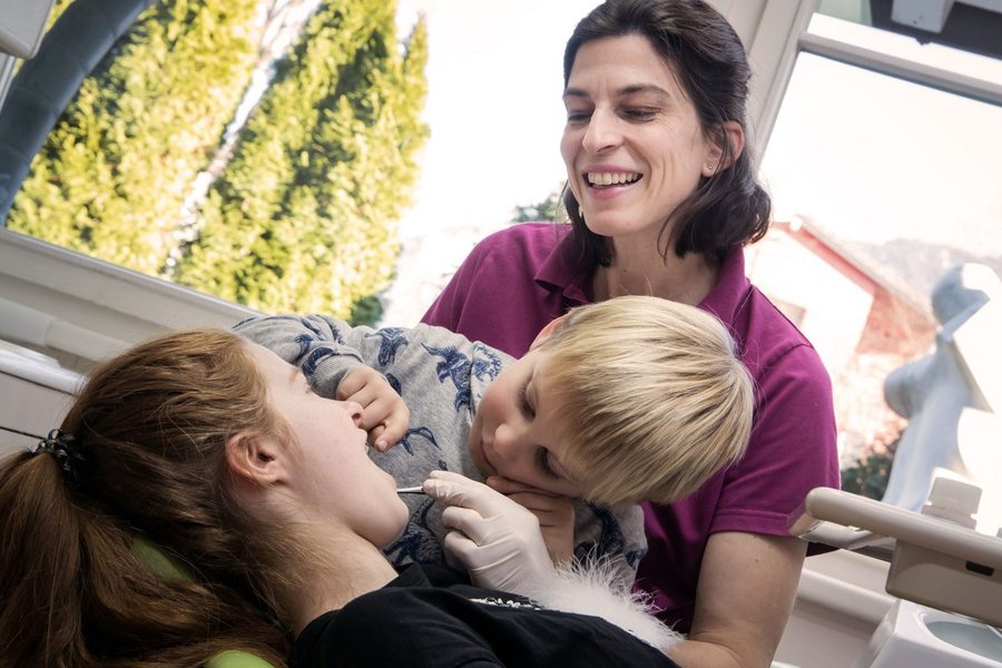 Erster Zahnarztbesuch: ein Kind auf dem Behandlungsstuhl neben einer Mitarbeiterin